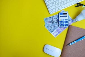 Blank notebook with a pen sits on an office desk table surrounded by computer tools and a range of materials. background in finance and banking, flat lay, top view photo