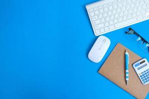 Blank notebook with a pen sits on an office desk table surrounded by computer tools and a range of materials. background in finance and banking, flat lay, top view photo