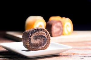 cierre un delicioso pastel de chocolate con crema batida en un plato cuadrado blanco sobre una mesa de madera en la cocina de la casa con un fondo negro y espacio para copiar. concepto de panadería casera. foto