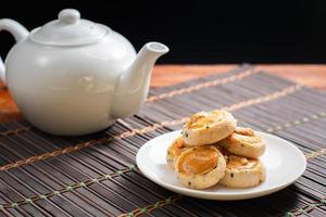 nuez de cajú y galletas de sésamo negro en un plato blanco y una mesa de madera con una taza de té borrosa en el fondo negro. concepto de té de la tarde. foto