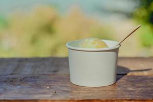 Delicioso helado de aguacate en tazón de papel blanco con cuchara de madera en la mesa con espacio para copiar el texto. reducir el concepto de plástico. foto