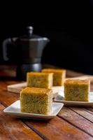 Close up square cut of homemade sweet and solf banana cake on white plate on table with solf focus black moka pot. Delicious and healthy bakery. photo