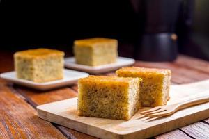 Close up square cut of homemade sweet and solf banana cake on wooden chopping board and fork on table. Delicious and healthy bakery. photo