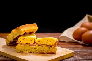 Waffle sandwich with egg and chicken ham on chopping board on wooden table and black background. Homemade food concept. photo