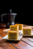 Close up square cut of homemade sweet and solf banana cake on white plate on table with solf focus black moka pot. Delicious and healthy bakery. photo