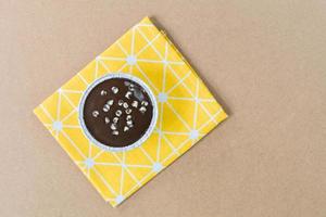 Top view dark chocolate cake with chocolate chips topping in round foil cup on yellow tablecloth and wooden table. Copy space for your text. photo