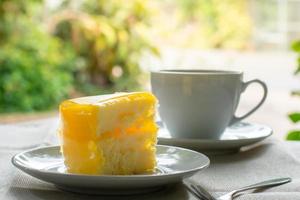 Delicious slice of orange cake served on white dish in coffee times on tablecloth. photo