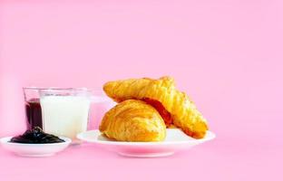 croissants servidos con un vaso de leche fresca, café sobre fondo rosa. concepto de desayuno. foto