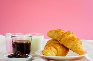 croissants served with glass of Fresh milk, coffee on pink background. Breakfast concept. photo