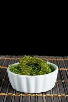 Fresh sea grapes or caviar seaweed in white bowl on wooden mat and black background. Healthy food concept. photo