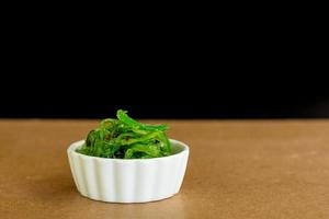 concepto de comida japonesa. Ensalada de algas frescas con semillas de sésamo en tazón blanco sobre fondo negro. foto