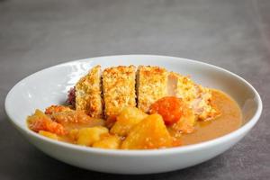 Japanese curry with rice, carrot, potato and deep fries chicken in white dish on table. photo