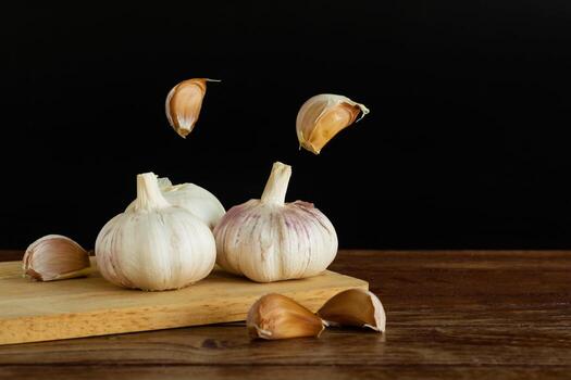 Group of garlic on chopping board and some garlic cloves floating in the air on wooden table with black background. Copy space for your text. photo