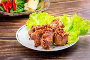 Thai deep-fried crispy pork with herb on white plate and wooden table. Food concept. photo