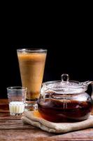 Transparent teapot with hot tea on brown cloth with glass of milk on  wooden table on black background with copy space. Famous beverage of Asian. Healthy drink concept photo