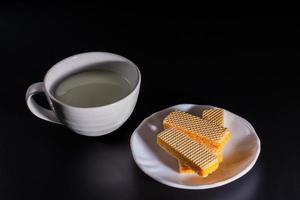 Side view four wafer in white plate with cup of milk on black background with copy space. photo