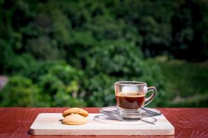 espresso o café negro servido con mantequilla borrosa y galletas de vainilla en una mesa de madera con fondo verde natural. bebida energética en el concepto de la mañana. foto