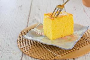 Piece of vanilla chiffon coconut cake on square plate on wooden table. Delicious small bakery for coffee and tea times. photo