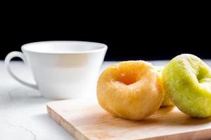 Vanilla and pandan doughnut on wooden chopping board with cup of hot milk. Breakfast concept. photo