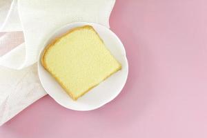 corte cuadrado de pastel de mantequilla de vainilla en plato blanco sobre fondo rosa. foto