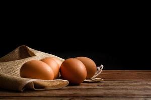 Group of chicken eggs with light bown table cloth on wooden table on black background with copy space.