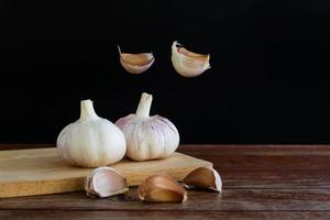 Group of garlic on chopping board and some garlic cloves floating in the air on wooden table with black background. Copy space for your text. photo