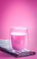 concepto de bebida de verano. leche rosa fresa con leche espumosa en vidrio transparente sobre fondo rosa. foto