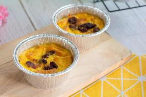 Bread pudding with black rasins in round foil cup on wooden tray. Delicious custard for coffee times. photo