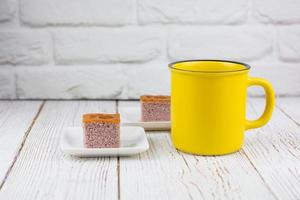 Yellow cup of fresh milk served with a square-cut of sweet potato cake on a white plate in the kitchen. Bakery and beverage concept. photo