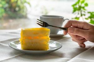 comer un trozo de tarta de naranja con un tenedor de metal servido en un plato blanco sobre manteles a la hora del café con un fondo de luz de naturaleza verde. foto