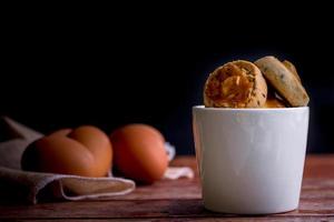 Cashew nut and black seasame cookies in white ceramic bowl on wooden table and blurry egg. Delicious snack for coffee time. photo