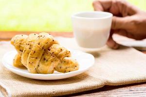 Breakfast concept. Croissants with perilla seeds on white plate and white cup of black coffee on wooden table with green bokeh background. photo