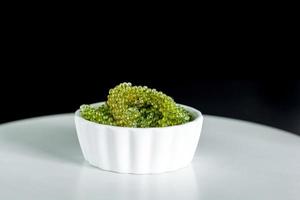 Fresh sea grapes or caviar seaweed in white bowl on black background. Healthy food concept. photo