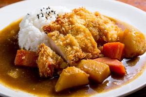 Japanese curry with rice, black sesame, carrot, potato and deep fries chicken in white dish on wooden table. photo