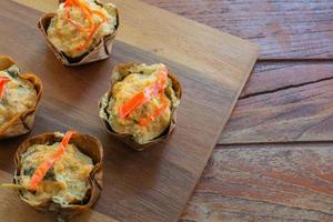 Thai steamed seafood curry in cup made from dry banana leave on wooden table and red chilli topping. Delicious Thai food. photo