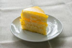 Delicious slice of orange cake served on white dish in coffee times on tablecloth. photo