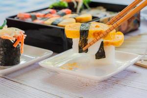 comiendo sushi tamagoyaki o huevo dulce sobre arroz y envoltura de algas en un plato cuadrado blanco con palillos. deliciosa comida japonesa. foto