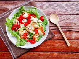 Healthy food concept. Grilled chicken breast salad with fresh red tomato, green lettuce, and mozzarella cheese on a white dish on wooden table. photo