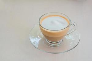 Layer of hot cappuccino coffee and milk froth in clear cup on wooden table in coffee shop.