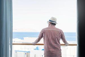 apuesto joven caucásico parado en el balcón del hotel, mirando la vista al mar foto