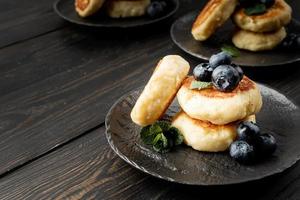 Cottage cheese fritters with blueberries on dark wooden background with copy space photo