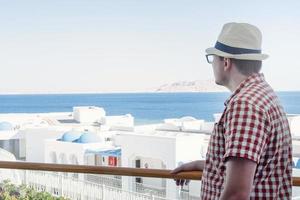 Handsome Caucasian young man standing on balcony of hotel, looking at sea view photo