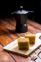 Close up square cut of homemade sweet and solf banana cake on wooden chopping board and fork on table with solf focus black moka pot. Delicious and healthy bakery. photo