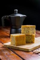Close up square cut of homemade sweet and solf banana cake on wooden chopping board and fork on table with solf focus black moka pot. Delicious and healthy bakery. photo