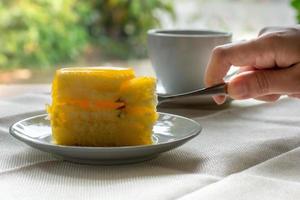 Eatting slice orange cake with metal fork served on white plate on table cloths in coffee times with green nature bokeh light background. photo
