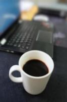 imagen borrosa de la taza de café y parte del teclado de la computadora en el entorno de la mesa de trabajo. negocio o financiero o tecnología o concepto de trabajo. foto