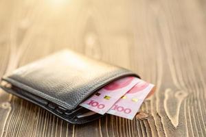 billetera de cuero negro con billete chino sobre mesa de madera foto