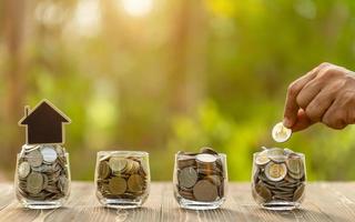 la varita pone una moneda en un frasco transparente sobre una mesa de madera. ahorro de dinero para el concepto de hogar foto