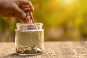 Vintage hourglass or sandglass and coin in clear glass jar on wooden table. Saving time and money concept photo