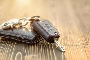 llaves de coche nuevas con billetera de cuero negro sobre mesa de madera. concepto de compra o alquiler de coches foto